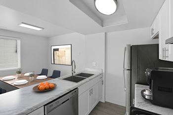 A kitchen with a refrigerator, sink, and a dining table set for two.